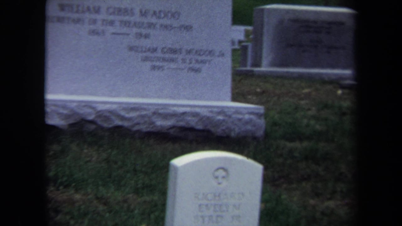 The 8mm frame shows the McAdoo headstone partly obscured by dark vertical shapes, with a smaller cemetery marker below.