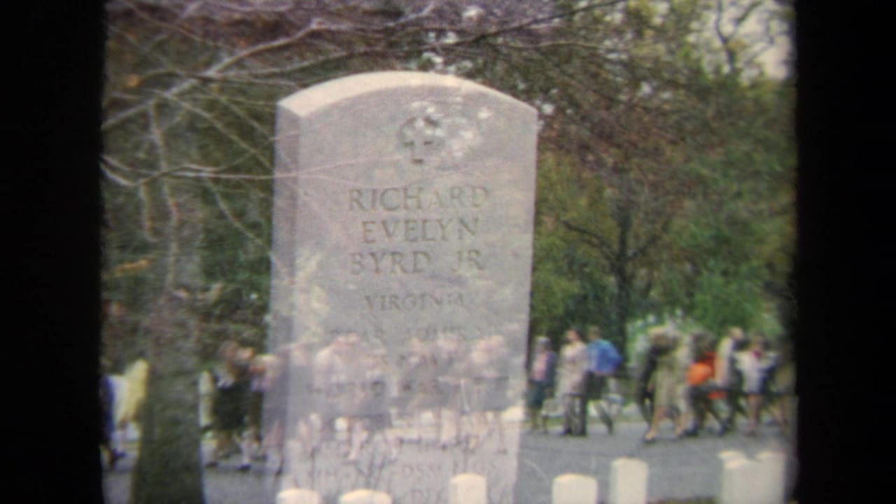 Gravestone seen through a dissolve or double exposure with people walking beyond it.