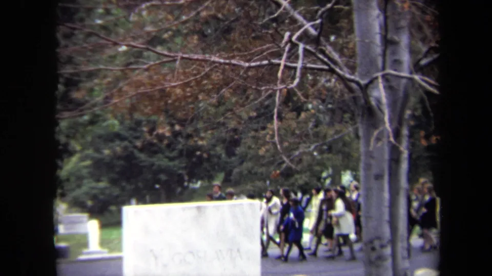 A wider cemetery frame shows walkers passing behind headstones beneath bare branches in Washington DC archival 8mm footage.