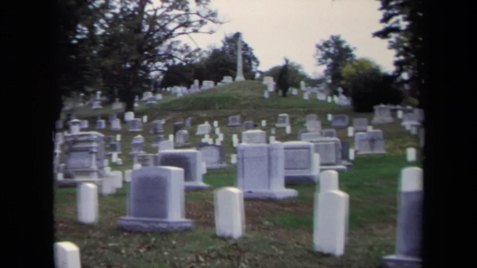1970 8mm cemetery pan in Washington, DC, with numerous headstones, grass, scattered leaves, and trees in soft focus.