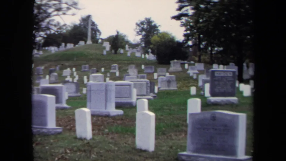 Final 1970 Washington, DC cemetery frame showing grave markers, a sloping lawn, mature trees, and a partially legible headstone.