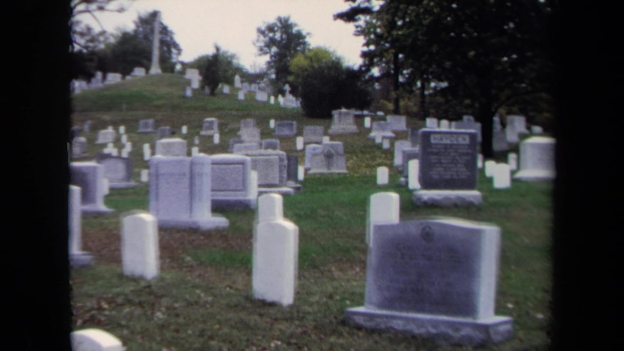 Wide cemetery view with rows of white headstones on a grassy hill.