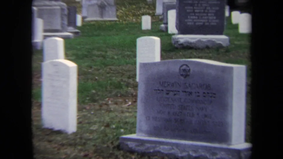 Closer 1970 Washington, DC cemetery frame showing a gray headstone, white markers, grass, and larger monuments in the background.