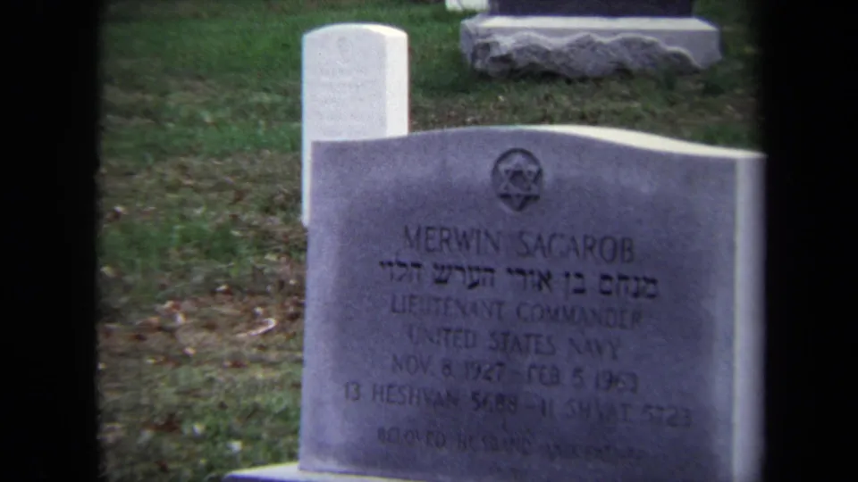 1970 Washington, DC frame zoomed on Merwin Sagarob's gravestone, showing Hebrew lettering, a Star of David, and U.S. Navy rank text.