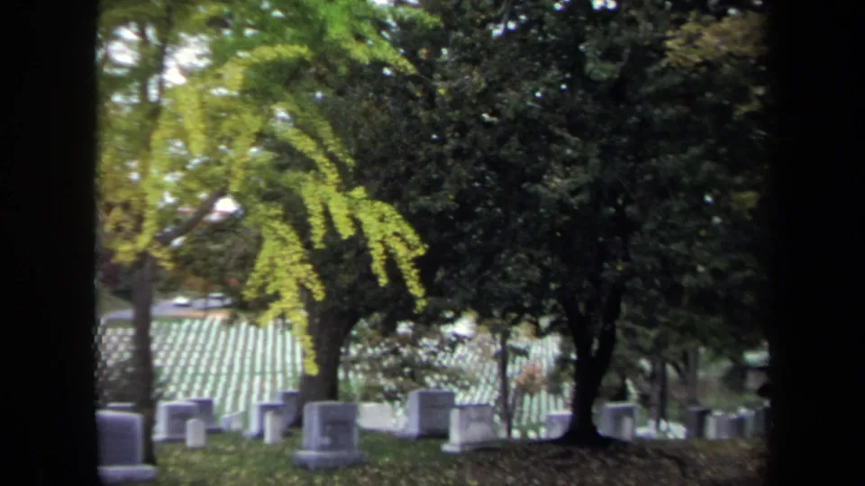 1970 Washington, DC cemetery view with rows of headstones, mature trees, fallen leaves, and dark film-frame edges.