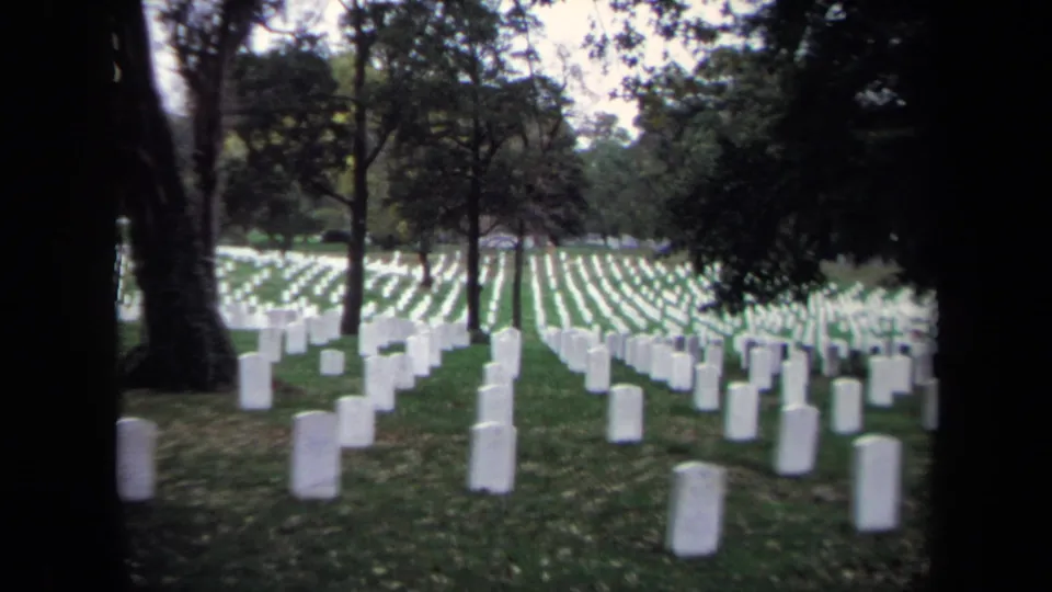 Rows of white headstones fill a Washington DC cemetery lawn, seen through trees in 1970 home-movie footage.