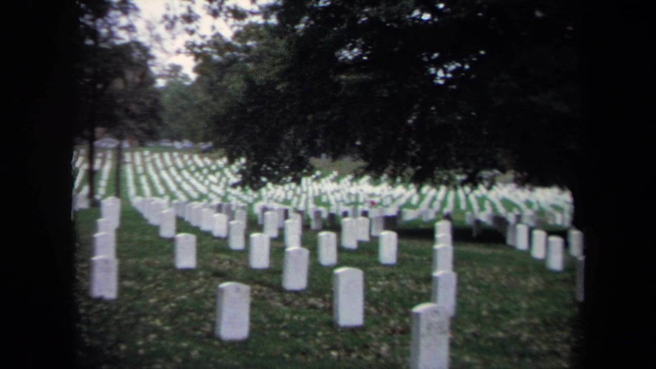 Rows of white cemetery headstones on green grass beneath dark trees.