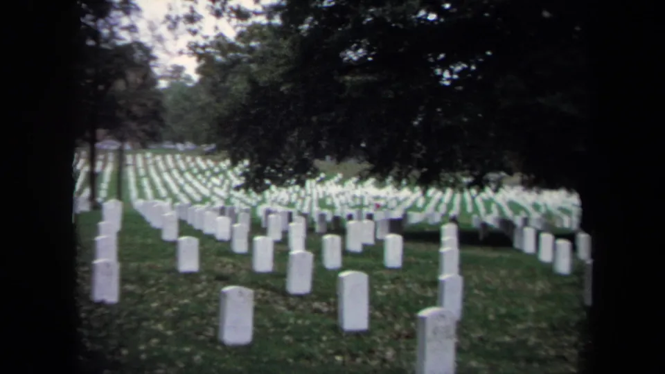 1970 Washington, DC 8mm view of white cemetery headstones receding across green grass under dense tree shade.