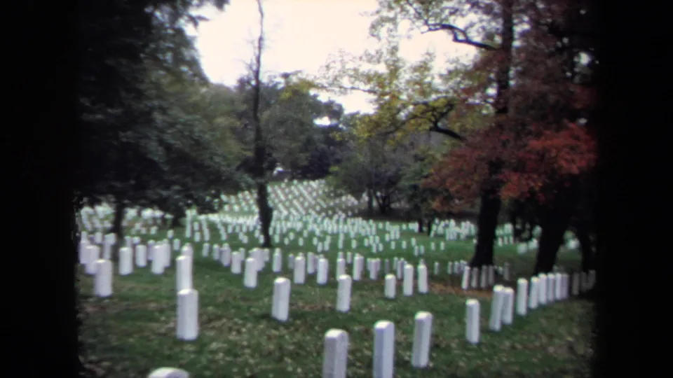 Rows of white tombstones in a Washington, DC national cemetery setting, framed by trees and early autumn color.