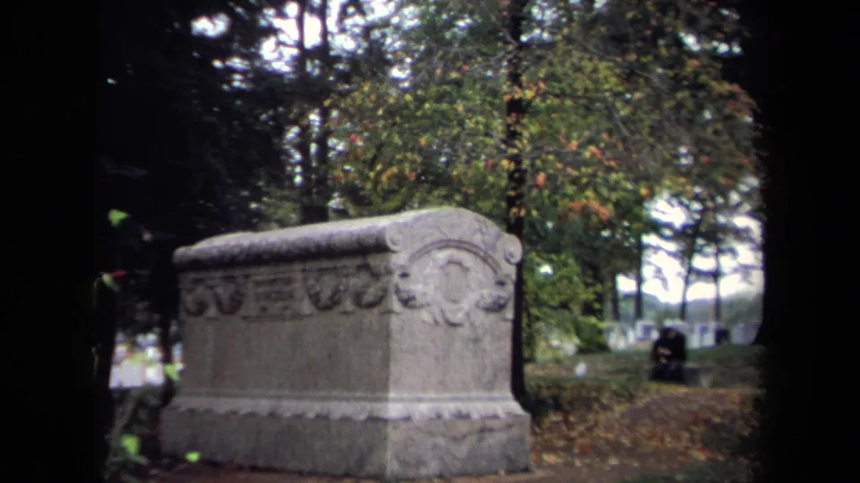 Close visitor-shot view of a large carved tombstone in a Washington, DC cemetery, with autumn trees and distant headstones.