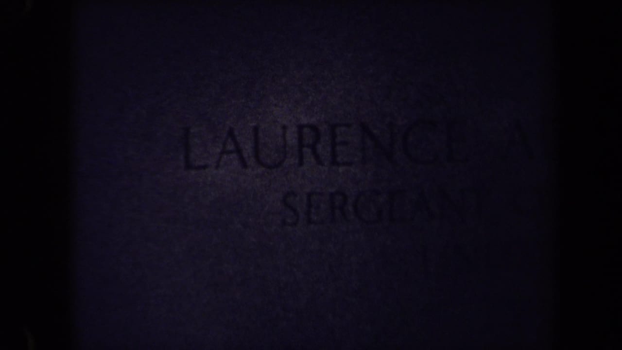 Dim close-up of a headstone with the name Laurence and part of the rank visible.