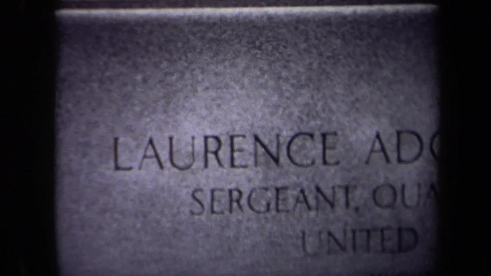 Close 8mm view of the Washington, DC grave marker inscription, with Laurence Adolph and military rank text partially legible.