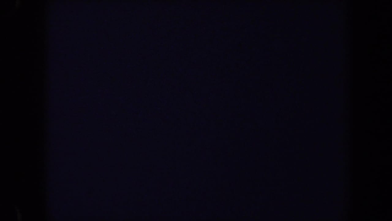 Mostly dark film frame with a faint cemetery view at the edge.