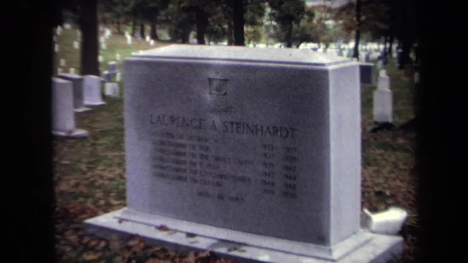 A stone grave monument appears in a Washington, DC cemetery, with trees, fallen leaves, and other headstones nearby.