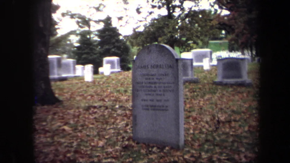 1970 Washington, DC cemetery view of James Forrestal's upright grave marker with leaves, grass, trees, and other headstones behind it.