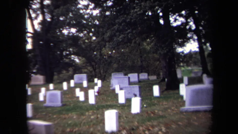 1970 Washington, DC 8mm view of white cemetery headstones among trees, with fallen leaves and dark frame edges.