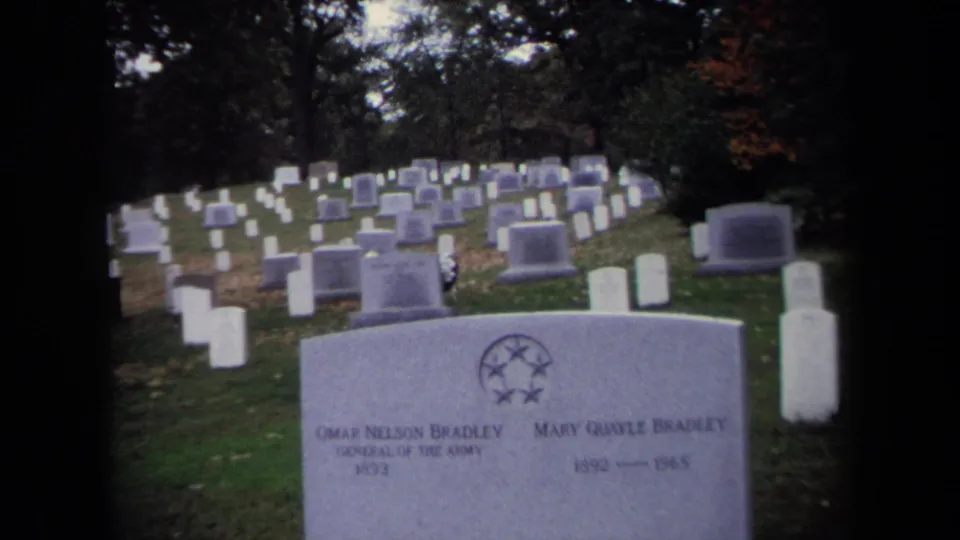 Wide 1970 8mm view of the Bradley grave marker on a grassy cemetery hillside with many white headstones behind it.