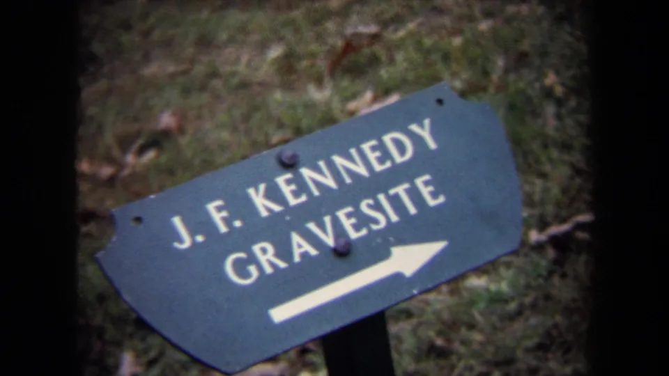 Another 1970 8mm view of the J.F. Kennedy Gravesite directional sign, with white lettering and arrow against a grassy cemetery setting.