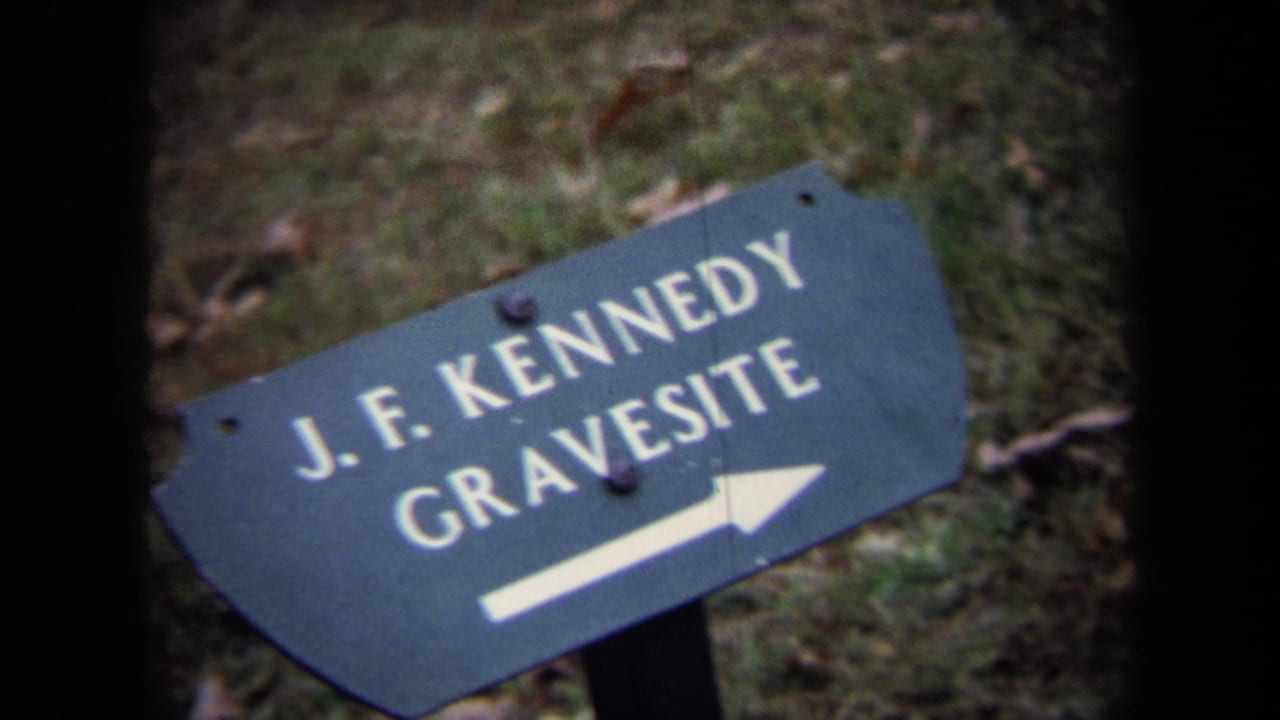 Dark blue sign pointing to the J.F. Kennedy gravesite on grass.