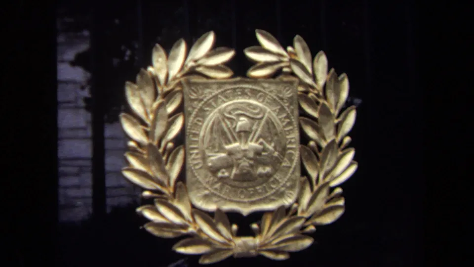 Close 1970 home-movie view of a gold laurel wreath around an official military-office seal on the Washington, DC gate.