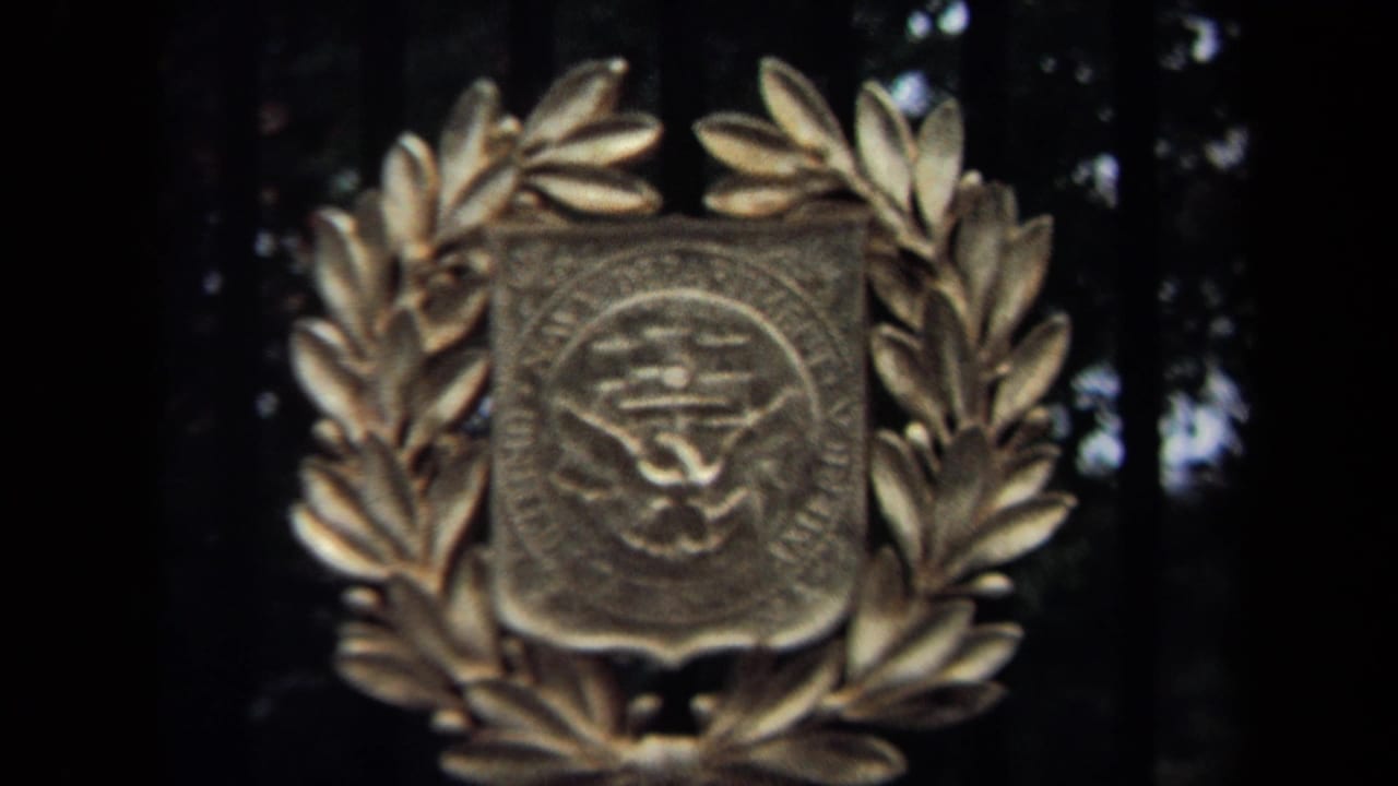 1970 Washington, DC home-movie frame with a metal government-style emblem centered inside a laurel wreath.