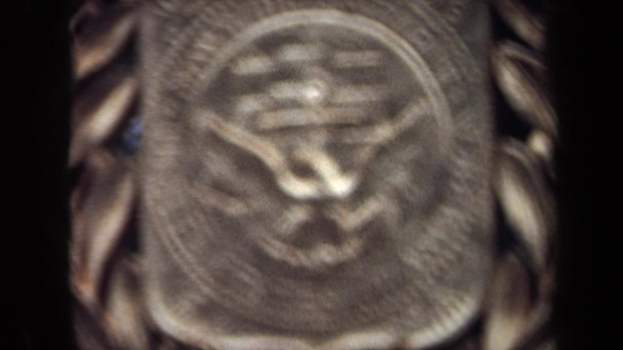 1970 8mm close-up in Washington, DC showing a blurred gold-toned medallion with a raised central symbol and laurel-like edge.
