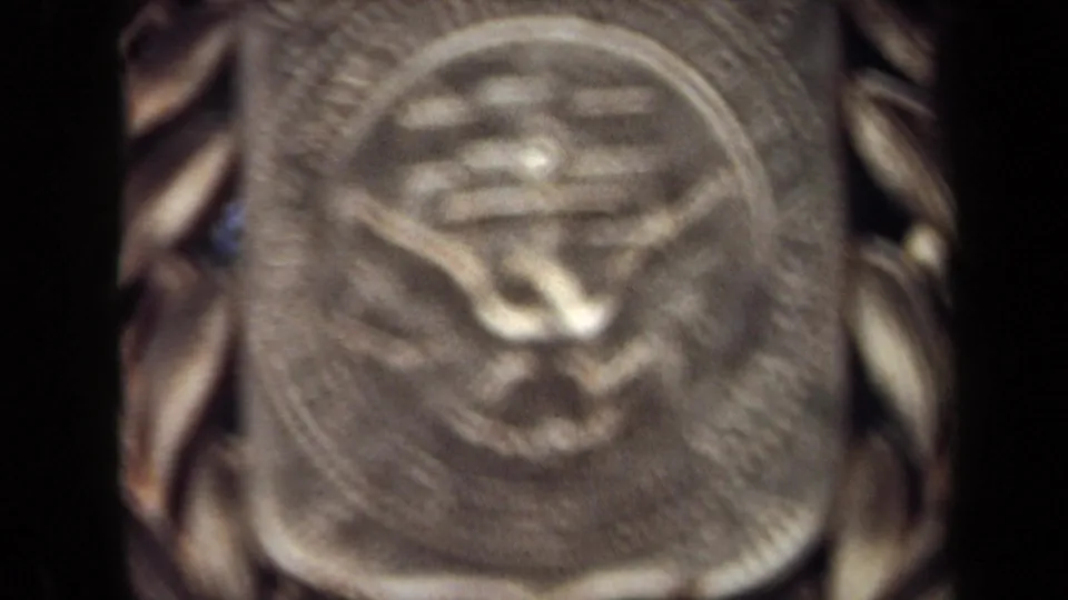 1970 8mm close-up in Washington, DC showing a blurred gold-toned medallion with a raised central symbol and laurel-like edge.