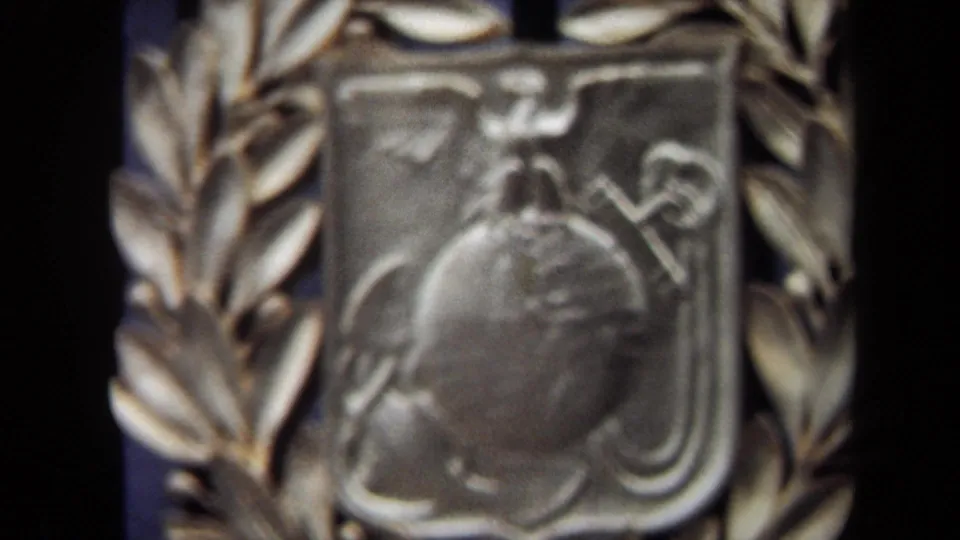 1970 Washington, DC 8mm frame of a gold-toned laurel-wreathed emblem, showing shield contours and a globe-like raised form.
