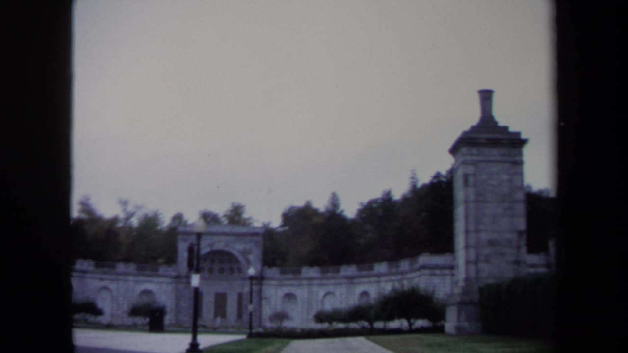 Stone gateway with arched openings, tower pier, trees, and a traffic light seen through dark frame edges.