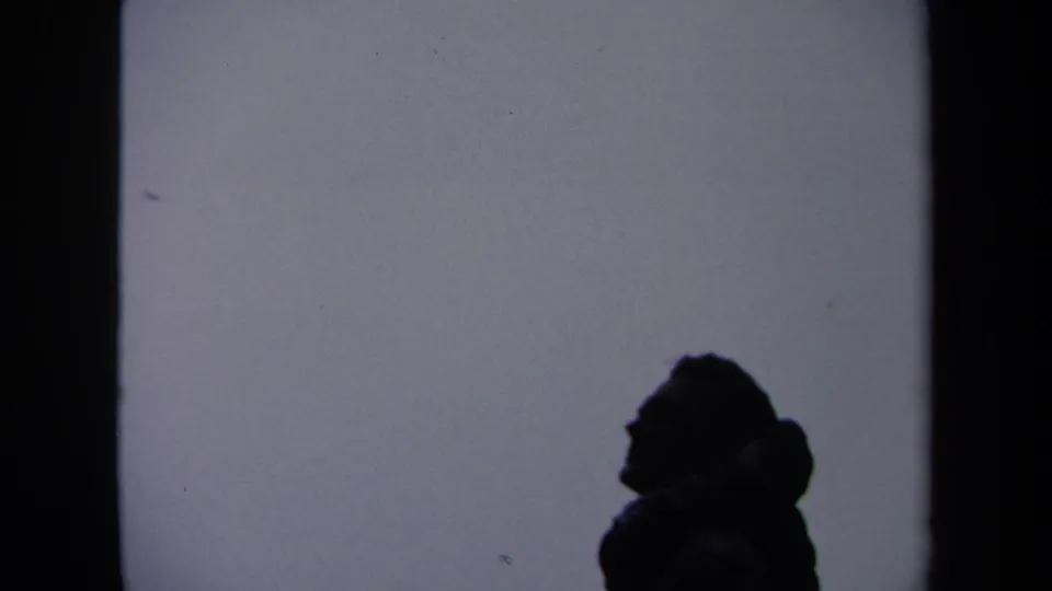 1970 Washington, DC home-movie frame showing a dark human profile silhouette against a pale wall surface.