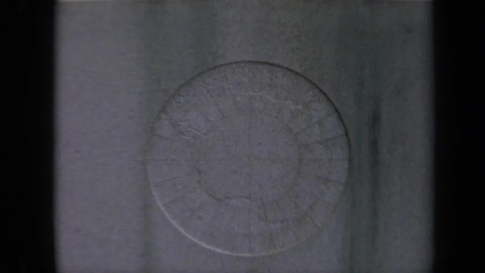 The zoom reveals more of the circular Arctic relief map, with faint lettering and embossed land outlines on a grainy 8mm frame.