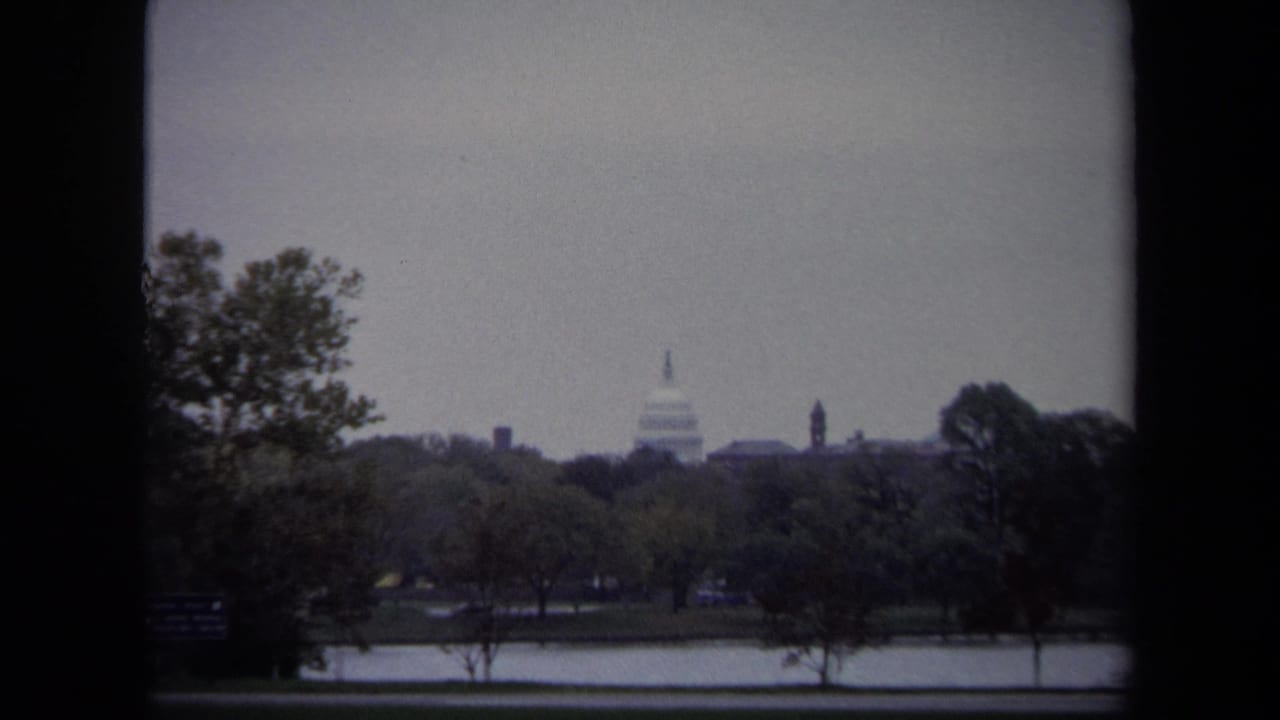 1970 Washington DC home-movie view of the U.S. Capitol dome seen across water and trees through dark 8mm frame edges.