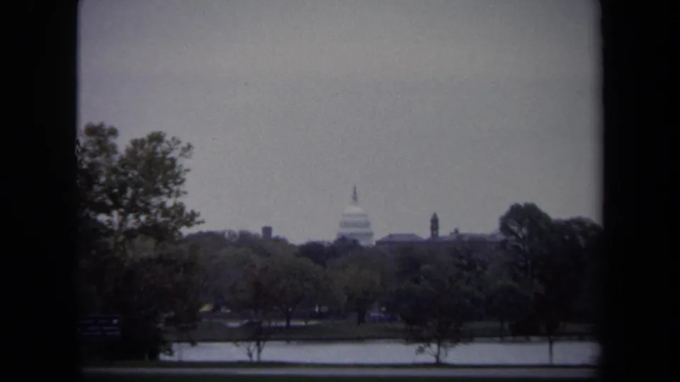 1970 Washington DC home-movie view of the U.S. Capitol dome seen across water and trees through dark 8mm frame edges.