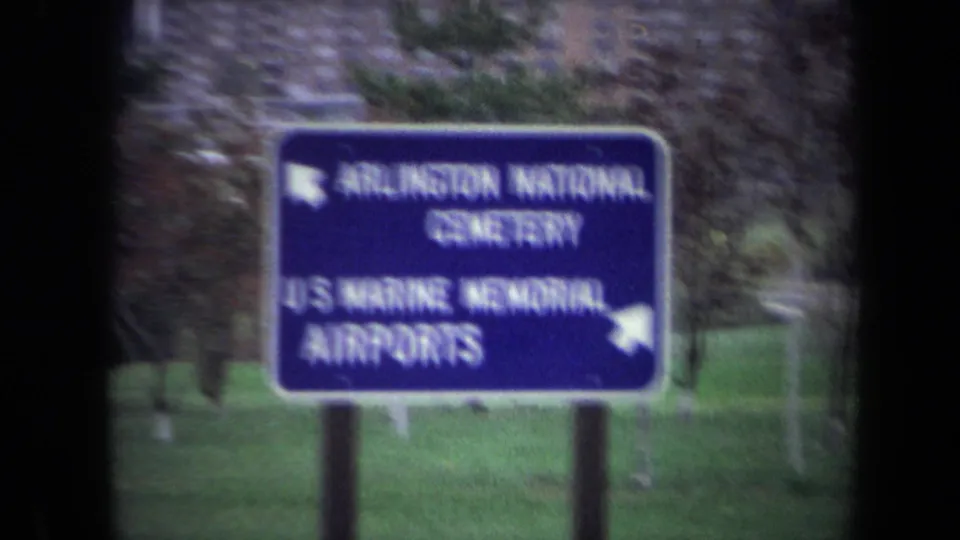 Motion-blurred 1970 Washington DC area roadside sign for Arlington National Cemetery, U.S. Marine Memorial, and airports near landscaped grounds.