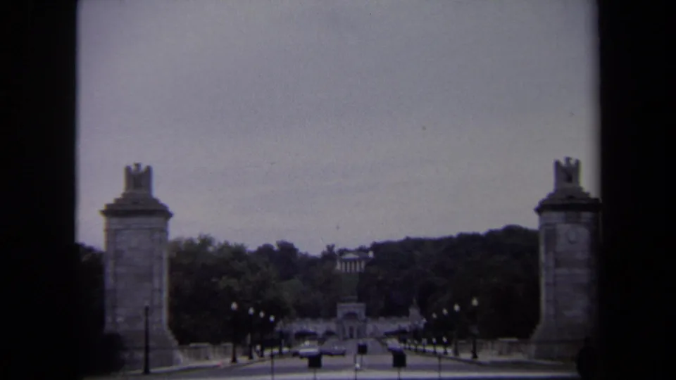 1970 Washington DC home-movie frame with stone pylons at the sides of a long road leading toward distant civic architecture.