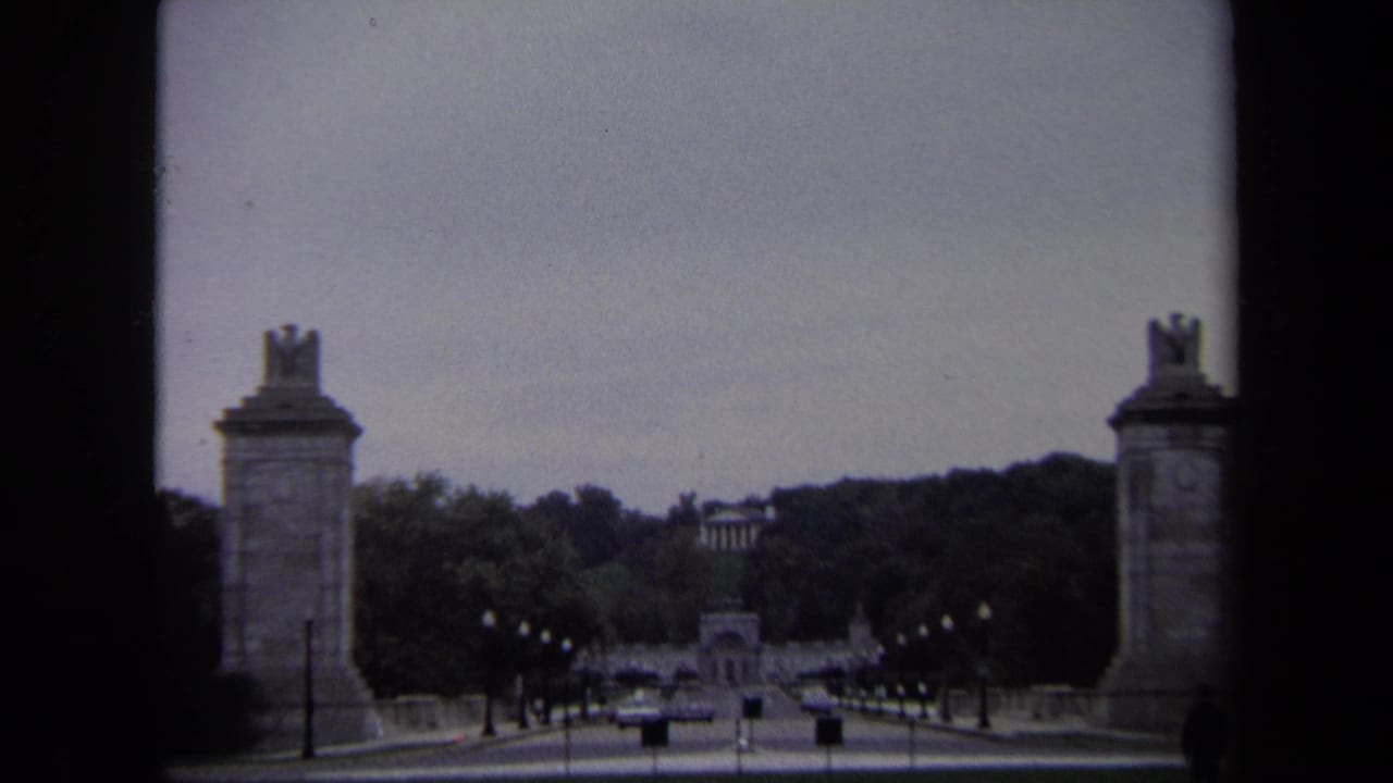 1970 Washington, DC 8mm frame showing eagle-topped stone pylons beside a road leading toward a distant neoclassical building.
