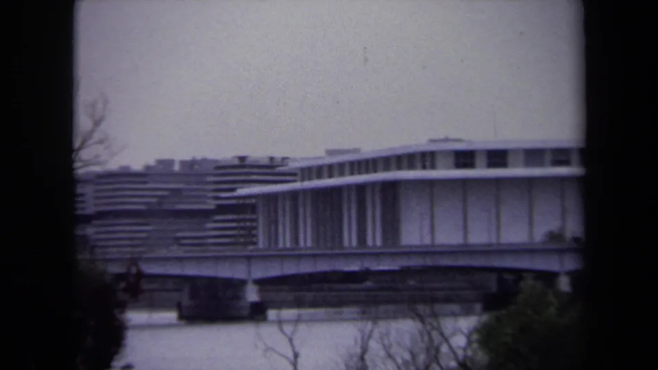 Closer 8mm frame of Washington, DC riverfront architecture, showing vertical supports, a bridge deck, and water below.