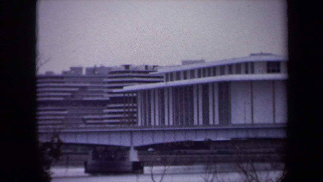 1970 Washington, DC home-movie frame showing a modernist building with horizontal lines, viewed through a dark window frame.