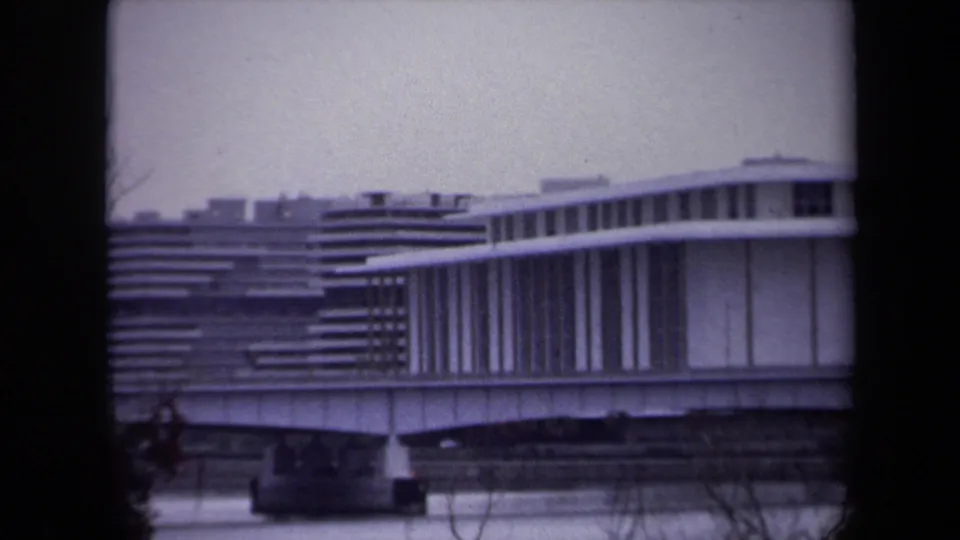 1970 Washington, DC home-movie frame showing a modernist building with horizontal lines, viewed through a dark window frame.