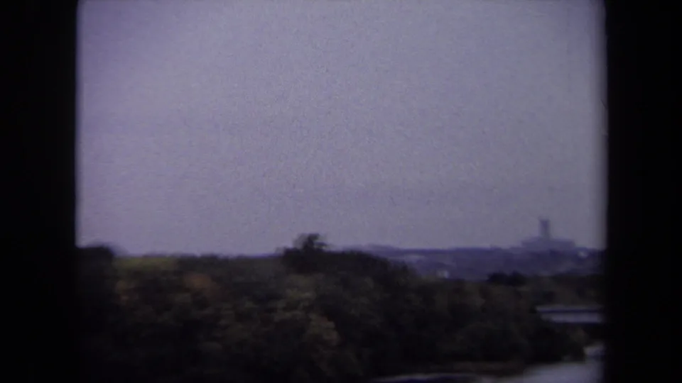 1970 Washington, DC home-movie frame with dark window edges, trees below, and a faint distant structure on the horizon.