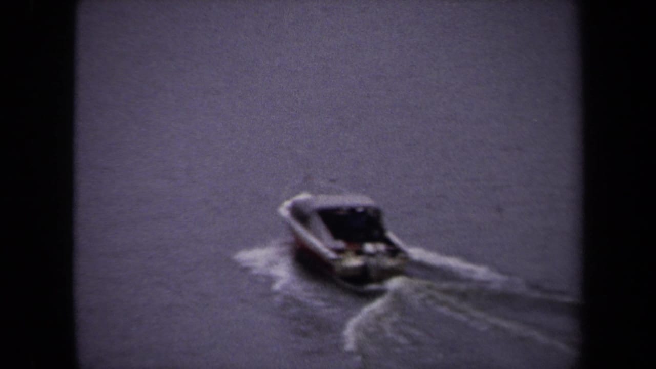 1970 Washington DC home-movie frame showing a small speedboat crossing a wide waterway, seen through soft 8mm grain.