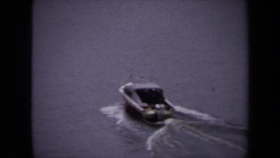 1970 Washington DC home-movie frame showing a small speedboat crossing a wide waterway, seen through soft 8mm grain.