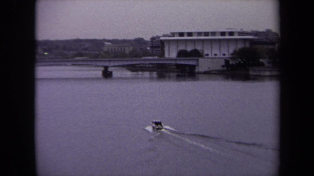 1970 8mm Washington, DC view of a small boat moving across water near a broad waterfront building and distant shore.