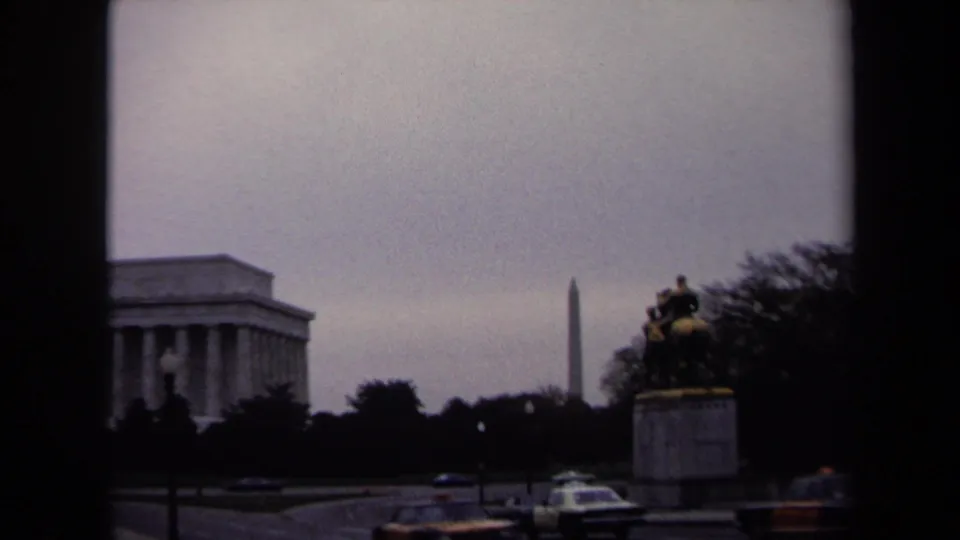Washington, DC landmark view with the Lincoln Memorial, Washington Monument, equestrian statue, and cars under an overcast sky.