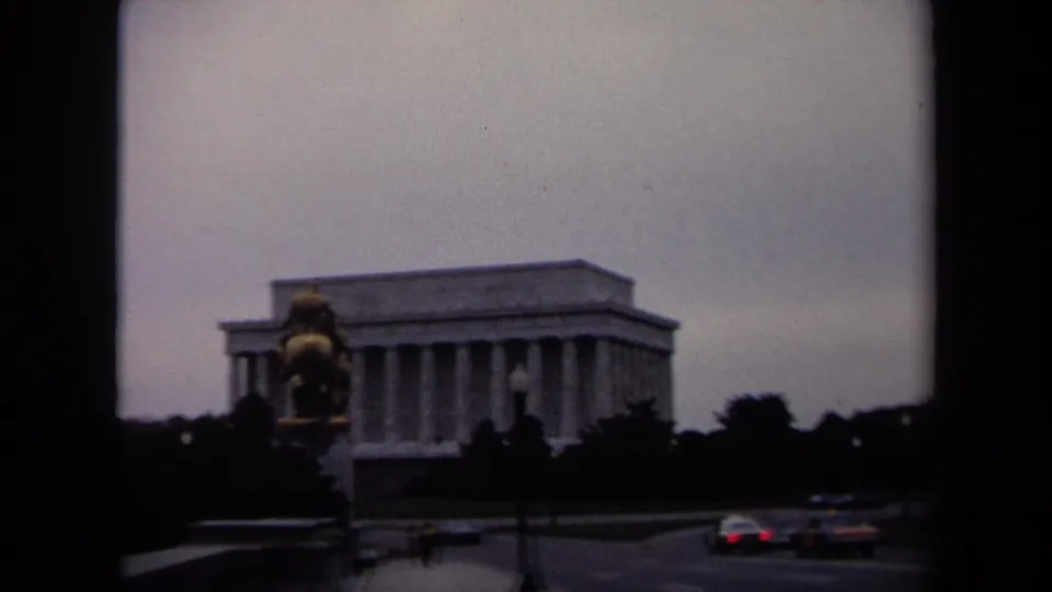 1970 8mm roadside view of the Lincoln Memorial partly framed by an equestrian statue and passing cars in Washington, DC.