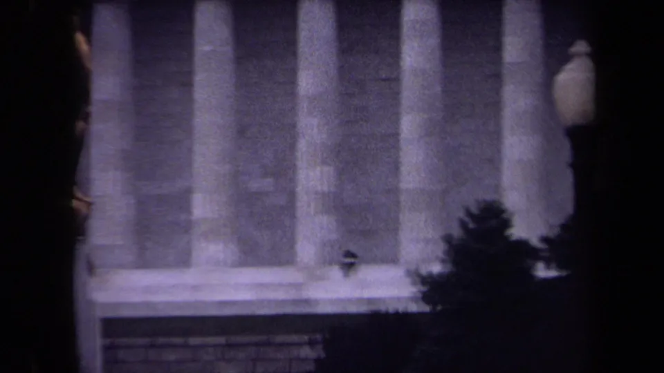 Zoomed 1970 8mm frame of the Lincoln Memorial columns and steps, with a small seated person visible near the base for scale.