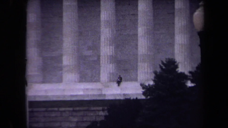 1970 Washington, DC home-movie frame focused on the Lincoln Memorial steps and columns, with a solitary seated visitor near the lower right.