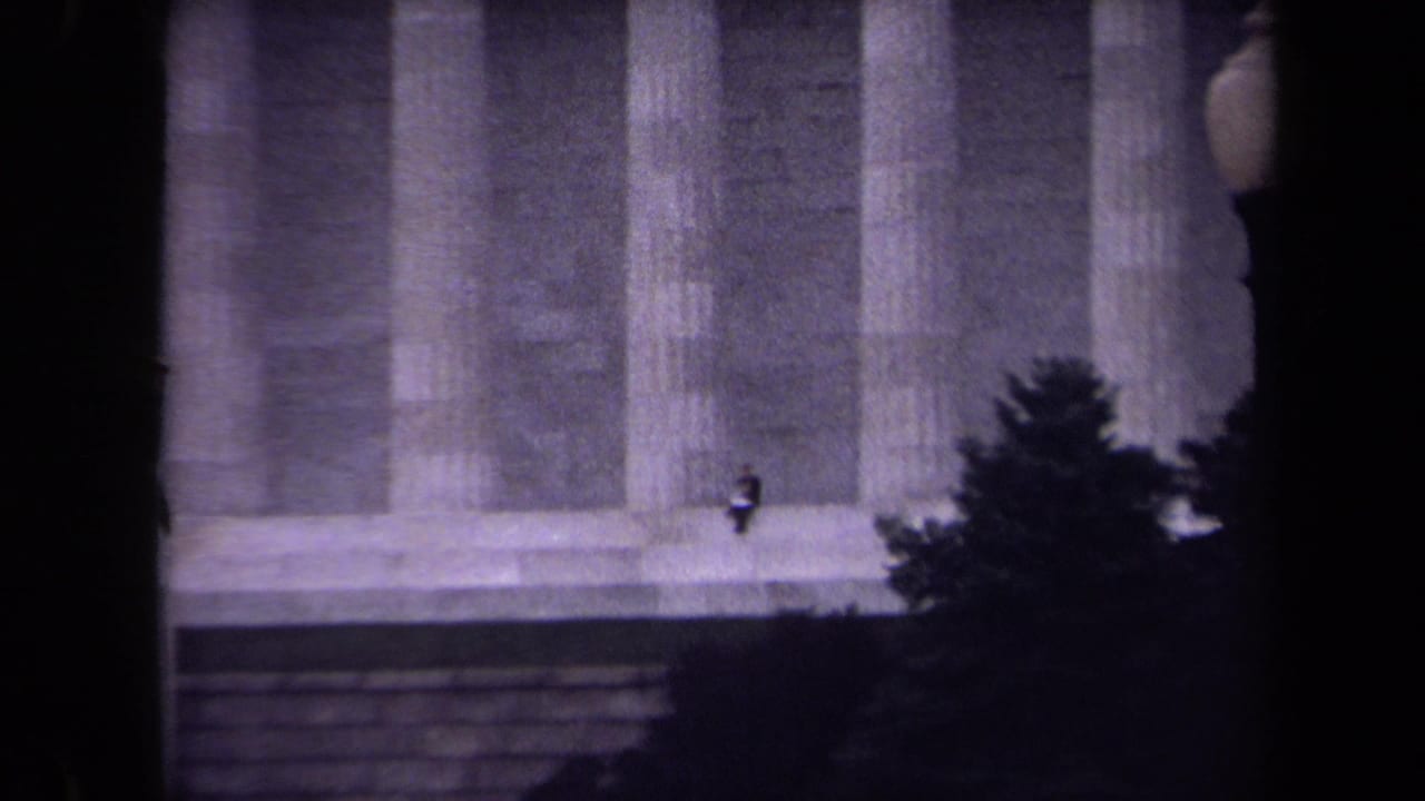 Large stone columns partly obscured by a tree and dark film edge.