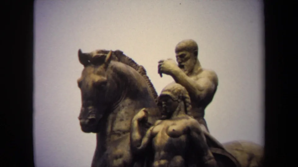 Close 8mm view in Washington, DC of a bronze equestrian sculpture with a rider and a female figure against a pale sky.