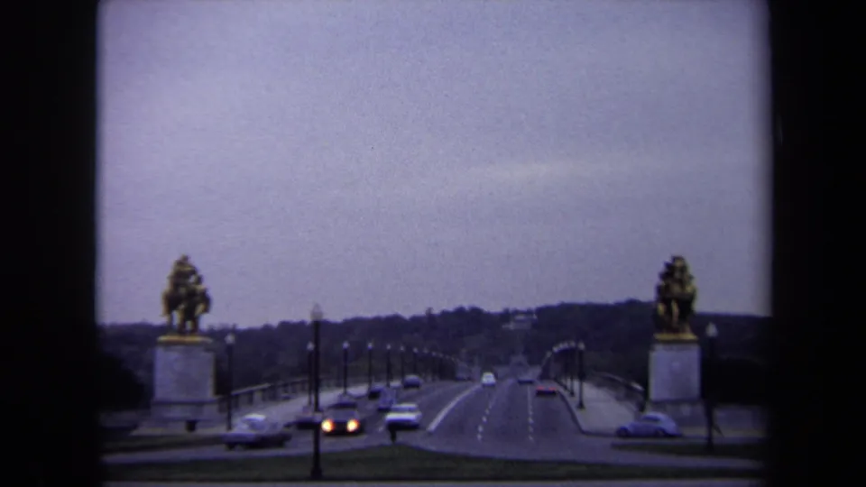 Wide Washington DC bridge view with cars traveling between two equestrian statues under an overcast sky.